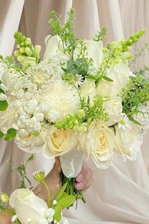 Bó hoa cưới rực rỡ và tinh tế, gồm những bông hoa tươi chọn lọc kỹ càng, thường là hoa hồng, baby, hoặc lan trắng, kết hợp hài hòa với lá xanh và phụ kiện nhẹ nhàng. Bó hoa được cắm khéo léo, vừa vặn, mang nét duyên dáng, lãng mạn, là điểm nhấn hoàn hảo cho ngày trọng đại của cô dâu.
