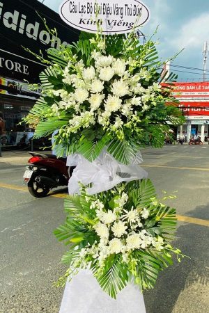 Lẵng hoa chia buồn với hoa cúc trắng, hoa lan trắng và lá xanh, mang thông điệp an ủi chân thành, được thiết kế tại shop hoa tươi Phú Giáo Bình Dương.